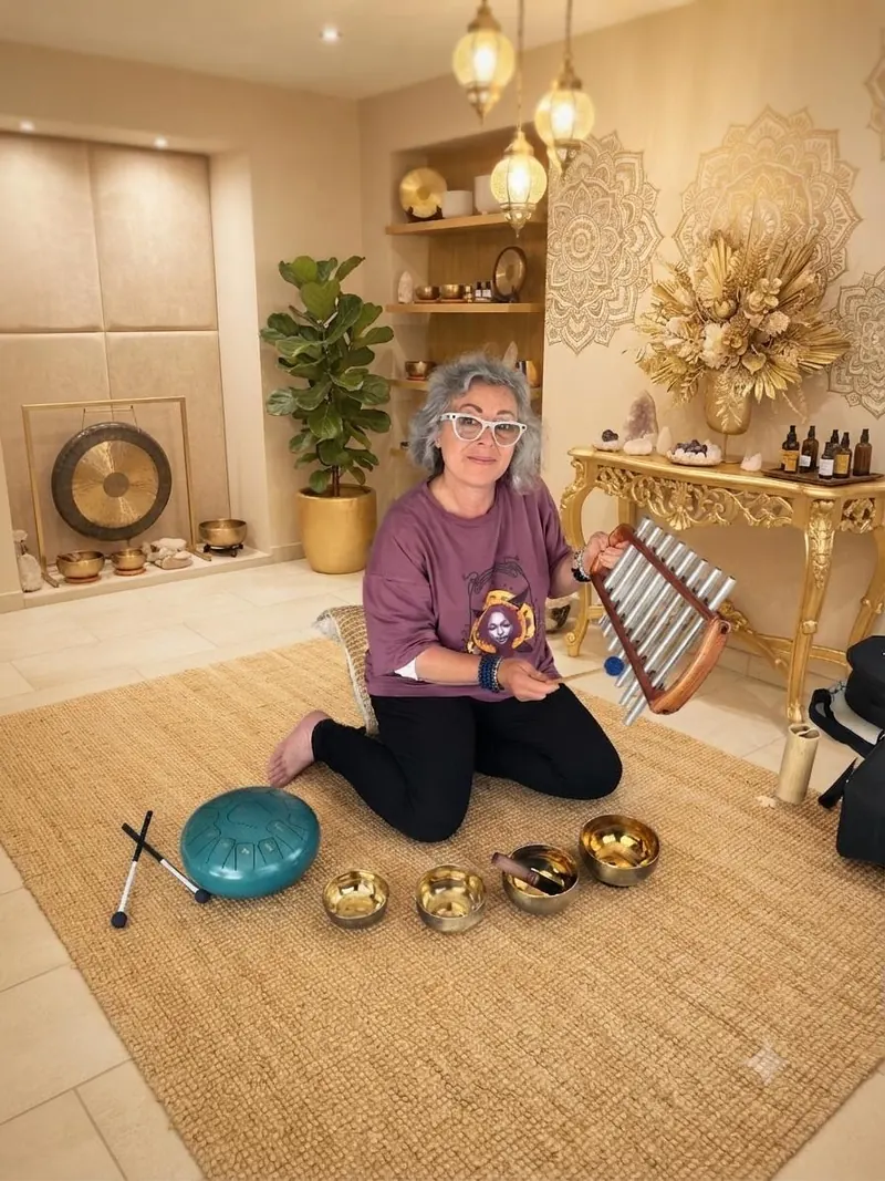 Derya assise parmi ses instruments, tenant un carillon à tubes métalliques